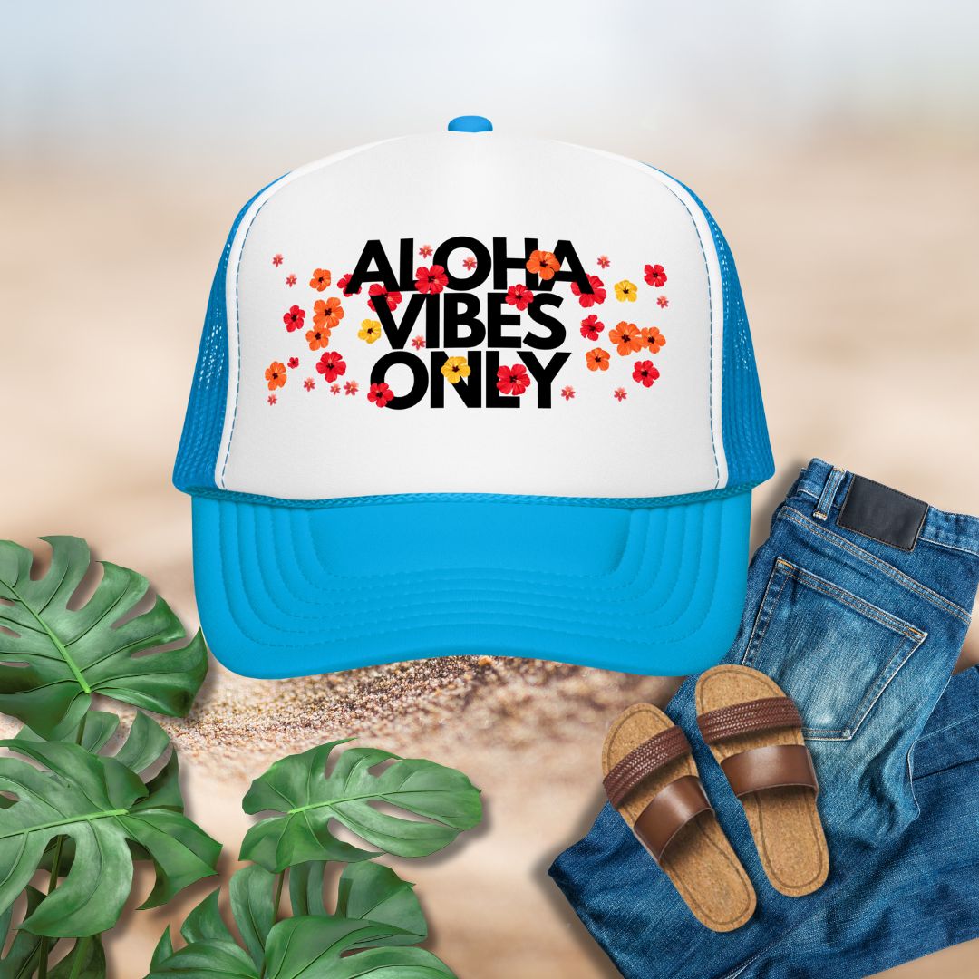 Blue and white cap with 'Aloha Vibes Only' text, sandals, jeans, and plants on a sandy background