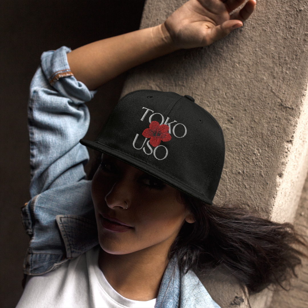 A person wearing a black snapback hat with 'TOKO USO' written in white on the front and a red logo on the side.