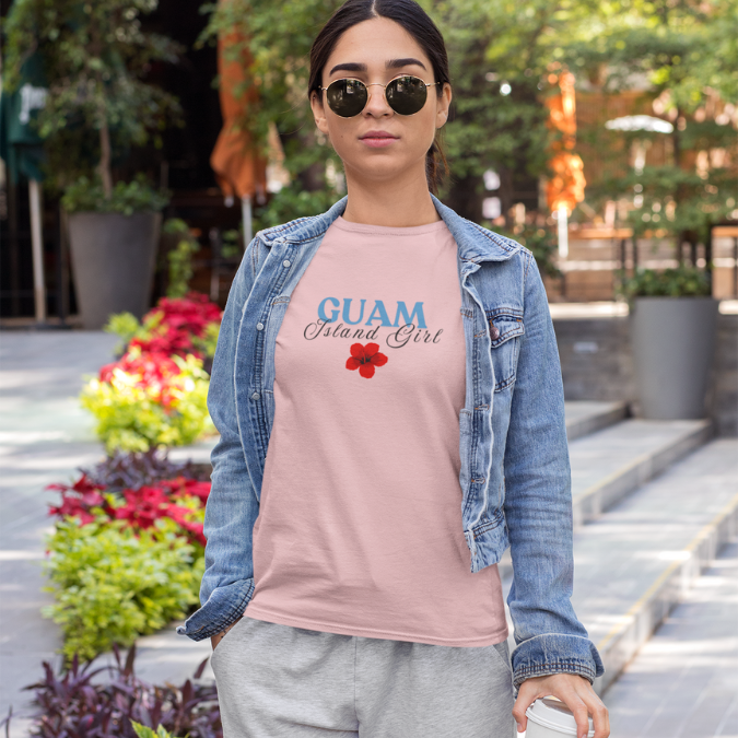 Woman wearing a pink 'GUAM Island Girl' t-shirt with a denim jacket outdoors.