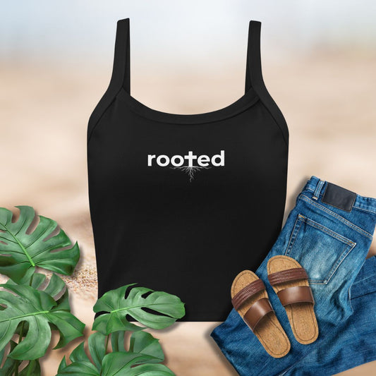 Black tank top with 'rooted' text, paired with jeans and sandals on a neutral background.
