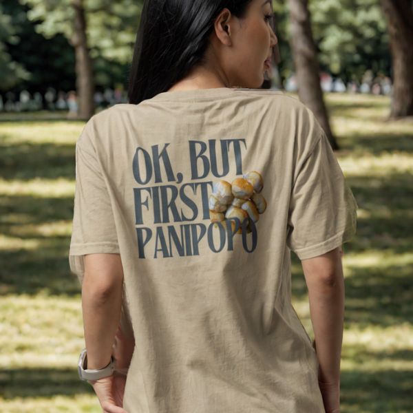 A person wearing a sport grey t-shirt with the text 'OK, BUT FIRST PANIPPOPO' printed on the back, featuring a graphic of a panipopo.