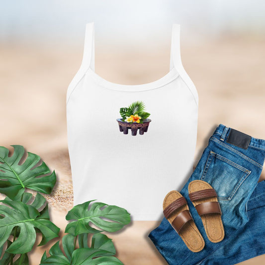 White tank top with a floral design, blue jeans, brown sandals, and green leaves on a neutral background