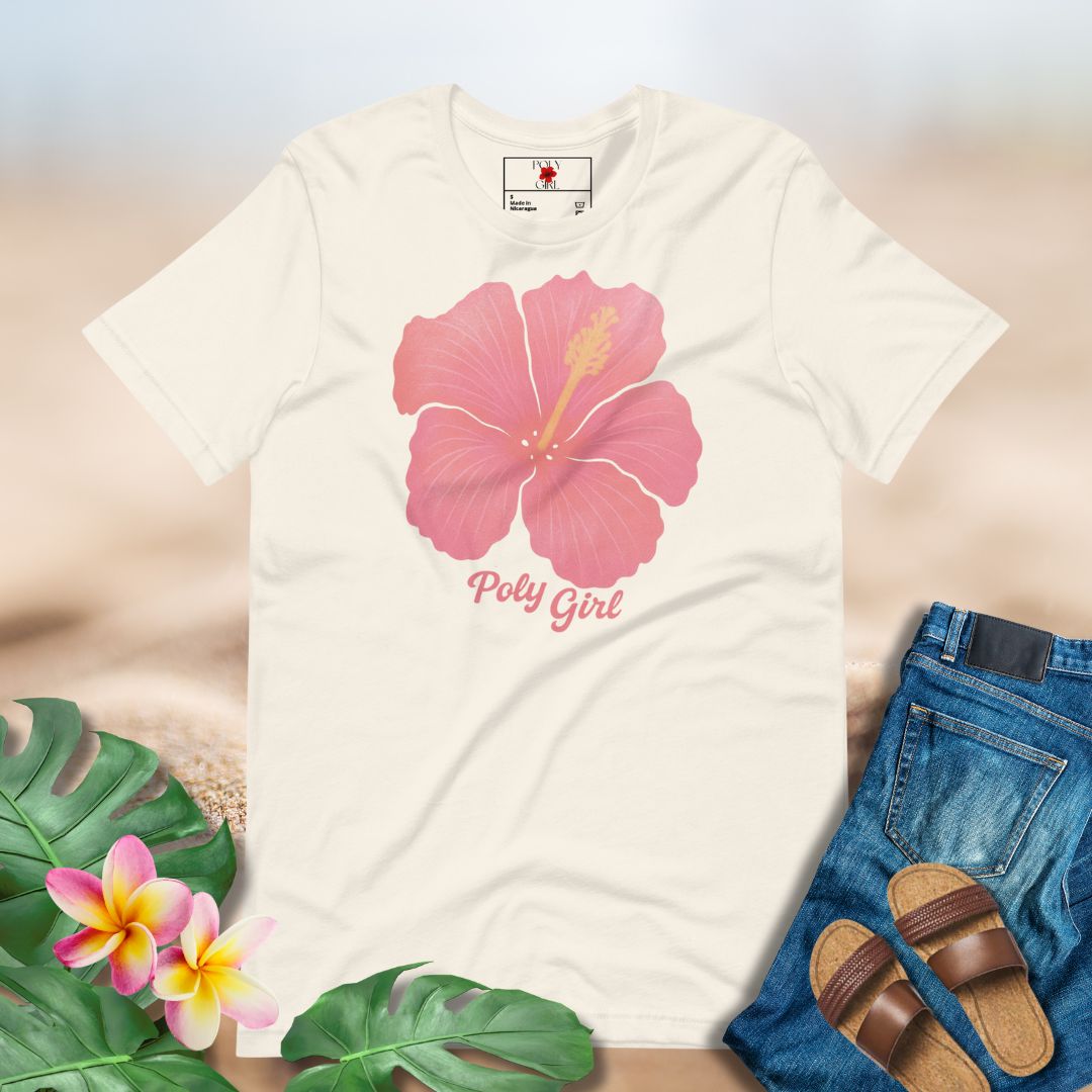 White t-shirt with pink floral design and 'Poly Girl' text, surrounded by tropical leaves and sandals.