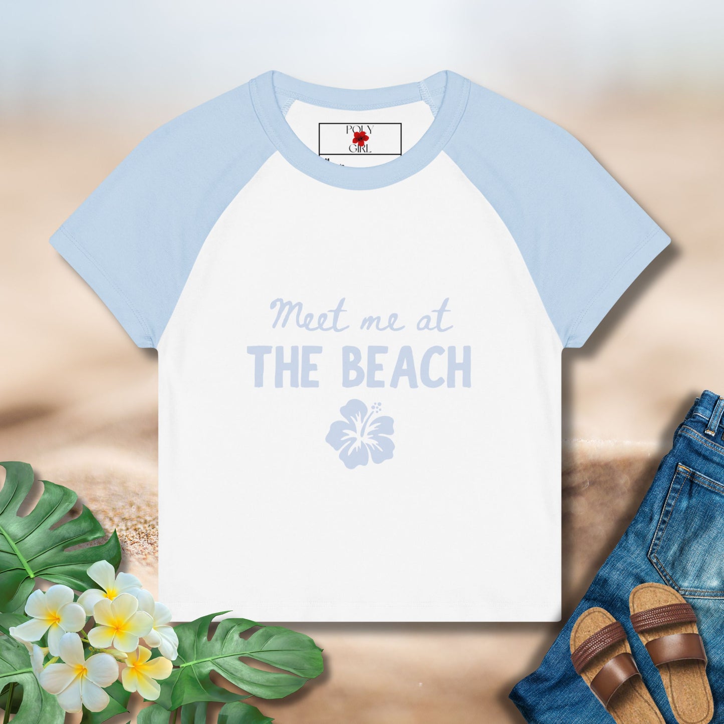 T-shirt with 'Meet me at THE BEACH' text on a sandy background with floral and shoe elements.