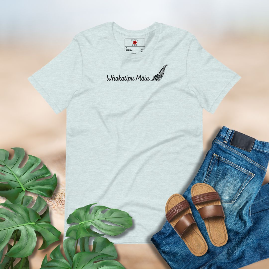 Light blue t-shirt with 'Whakatipu Maia' text, paired with jeans and sandals on a neutral background.