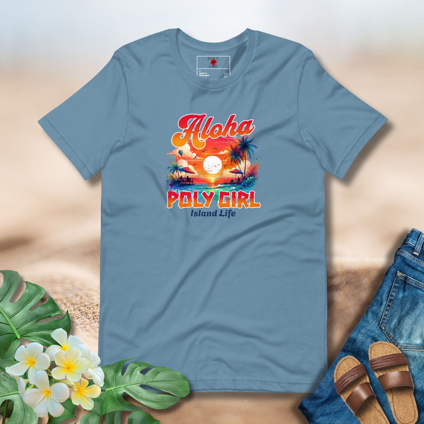 Blue t-shirt with 'Aloha Poly Girl Island Life' design on a sandy background with flowers and sandals.