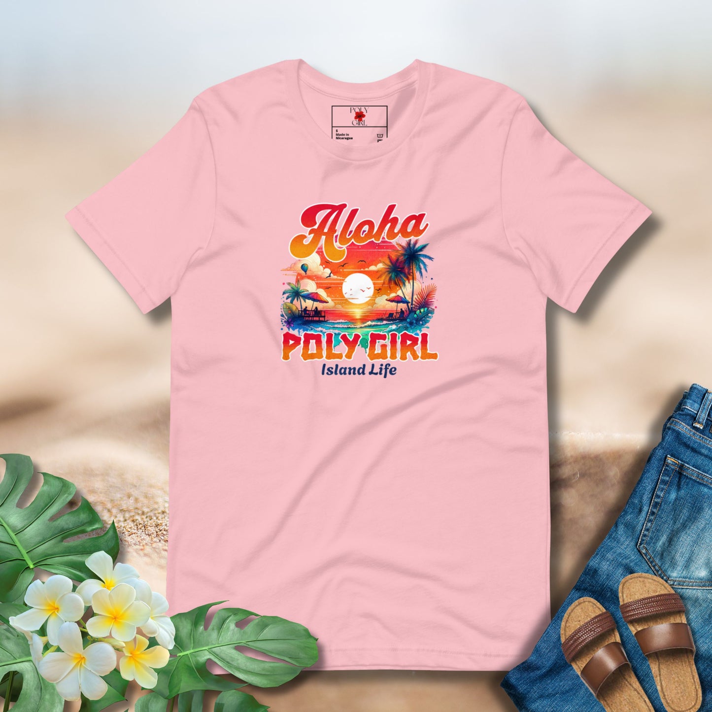 Pink t-shirt with 'Aloha Poly Girl' design on a sandy background with flowers and sandals.