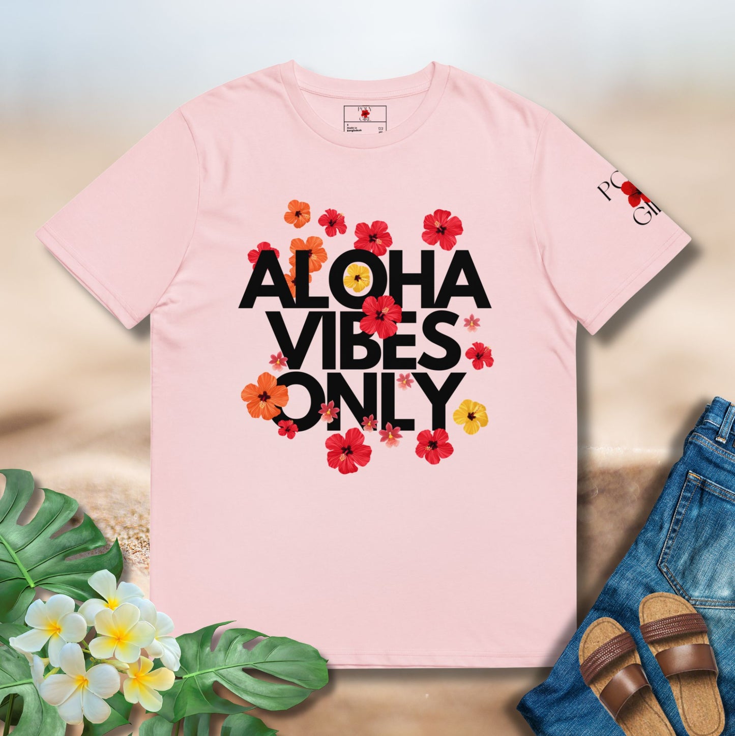 Pink t-shirt with 'Aloha Vibes Only' text and flowers on a sandy background with sandals and flowers.