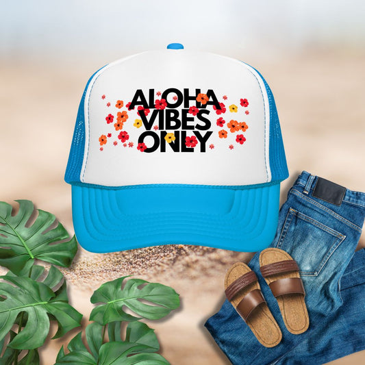 Blue and white cap with 'Aloha Vibes Only' text, sandals, jeans, and plants on a sandy background