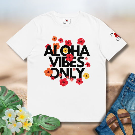 White t-shirt with 'Aloha Vibes Only' text and floral designs on a wooden surface with flowers and sandals.