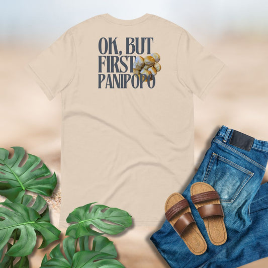 Beige t-shirt with text and graphics, paired with jeans, sandals, and green leaves on a light background