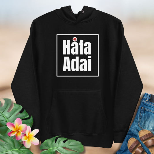Black hoodie with 'Häfa Adai' text on a neutral background with floral and clothing items.