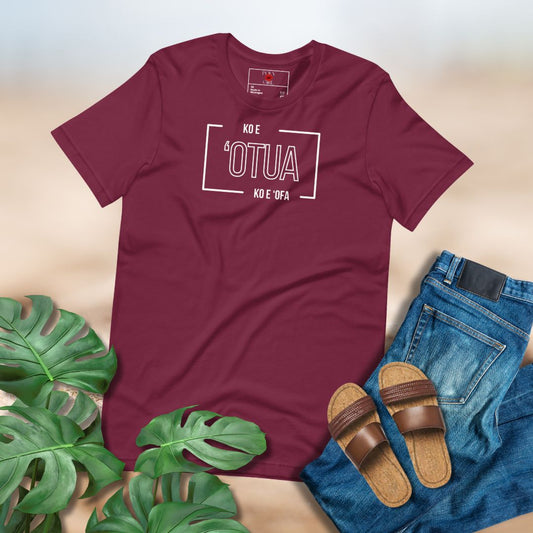 Maroon t-shirt with text "Ko e 'Otua Ko e 'Ofa" printed on front. Paired with sandals, jeans, and green leaves on a light background