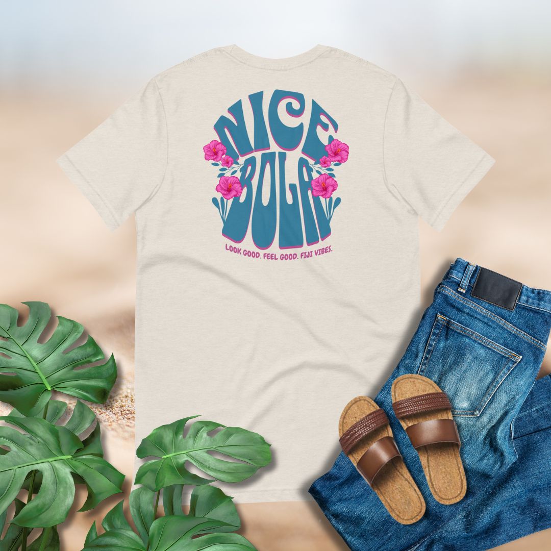 Beige t-shirt with 'Nice Bola' design, Fiji t-shirt design, surrounded by jeans, sandals, and green leaves on a light background