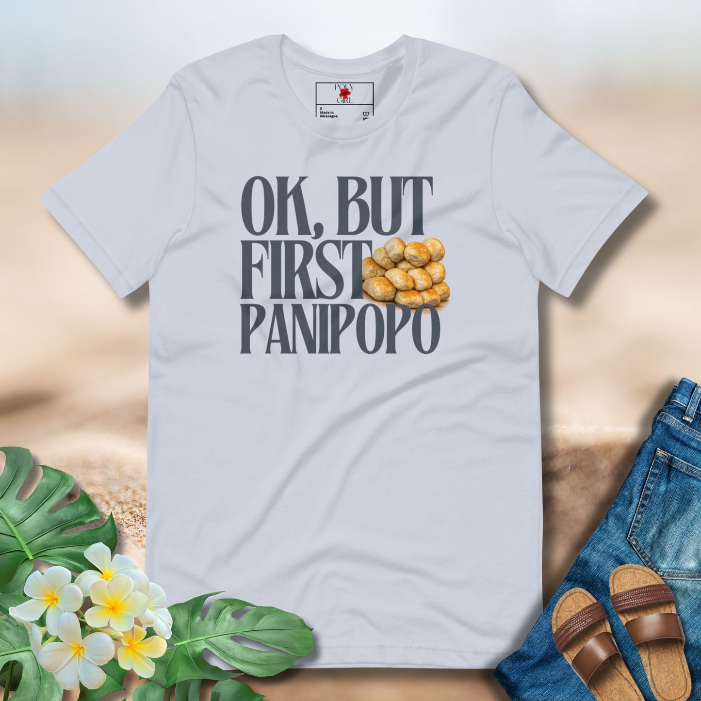 Light blue t-shirt with 'OK, BUT FIRST PANIPOPO' text and graphics on a neutral background with floral and denim elements.