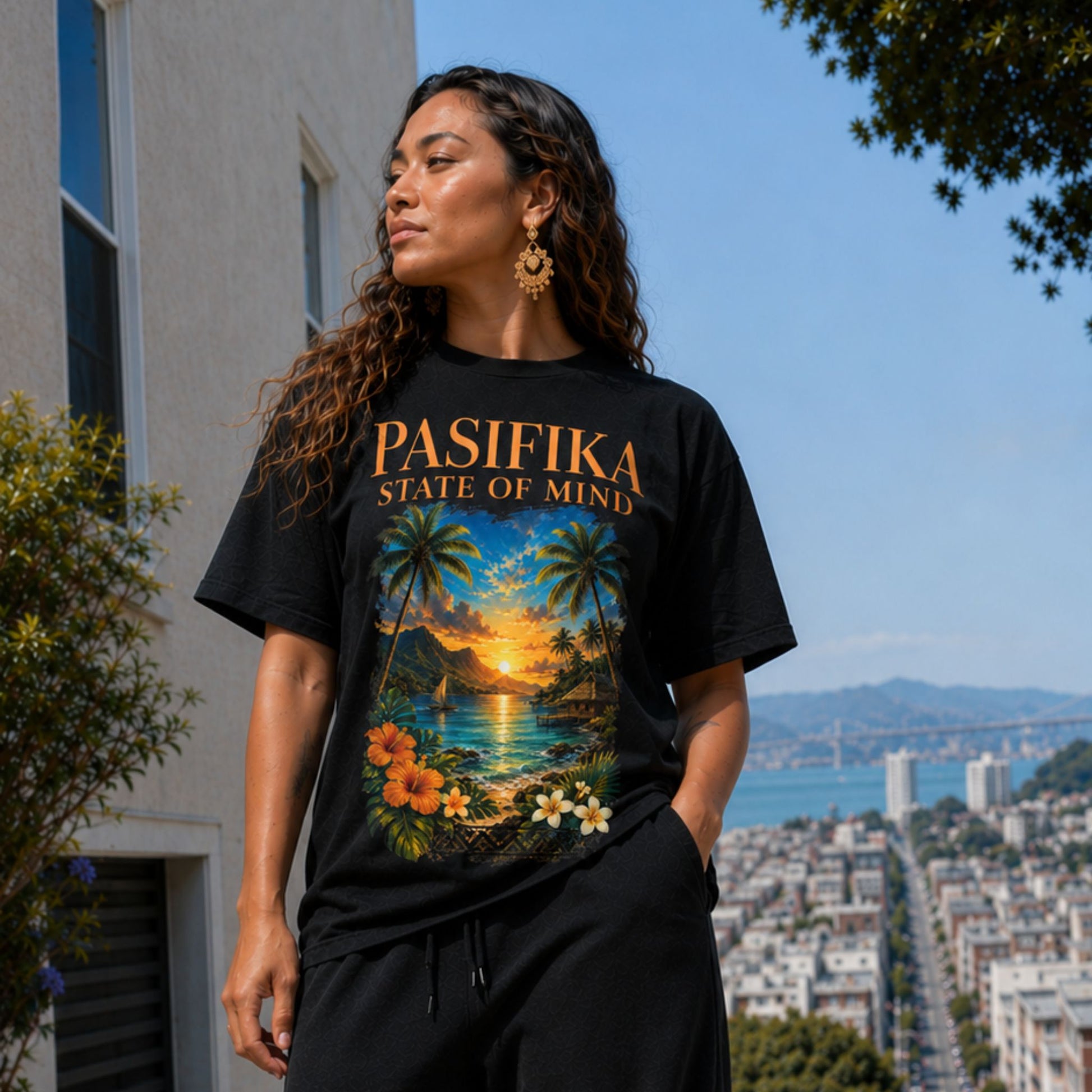 A woman wearing a black graphic t-shirt with 'PASIFIKA STATE OF MIND' and a tropical sunset print, standing outdoors with a city and bay view in the background.