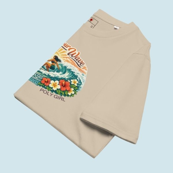 Folded tee featuring an island surf illustration with a woman riding a wave, tropical florals, sun, and Poly Girl logo.