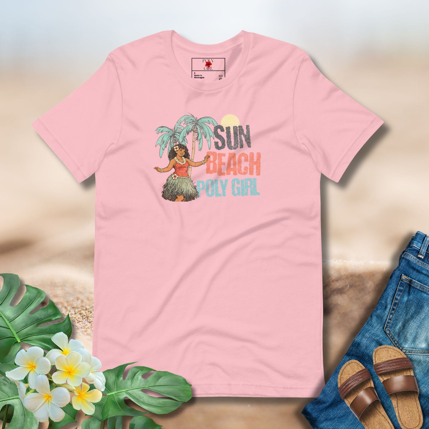 Pink t-shirt with a tropical design featuring a hula dancer, palm trees, and text on a sandy background.