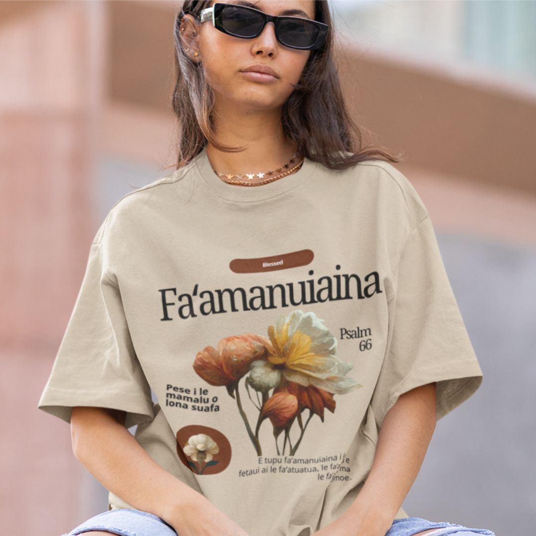A woman wearing sunglasses and an oversized beige t-shirt with a floral design and Samoan faith-based quotes.